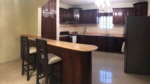 Una cocina con armarios de madera oscura, una isla central con taburetes de bar, un refrigerador y una araña.