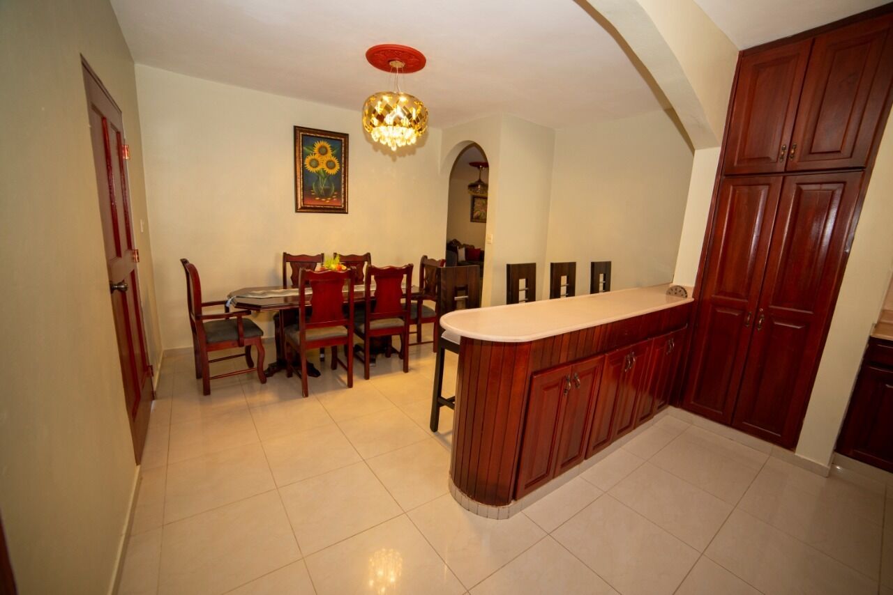 A kitchen with wooden cabinets, a white countertop, and a dining area with chairs and a table.