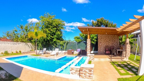 Un patio trasero con piscina, pérgola y zona de estar.