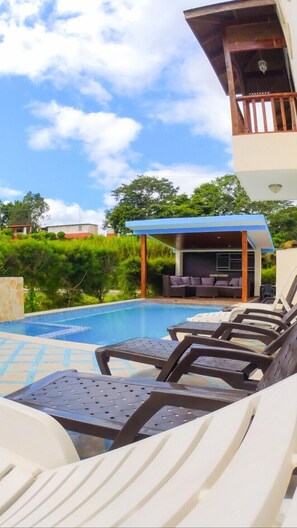 A poolside area with lounge chairs, a covered seating area, and a view of the surrounding landscape.