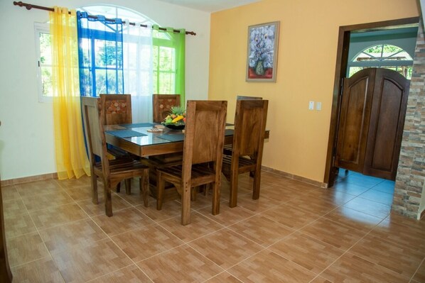 A dining area with a wooden table and chairs, a window with yellow curtains, and a door with a stone accent.