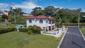 Une maison à deux étages avec un toit rouge, une piscine et une pelouse bien entretenue.