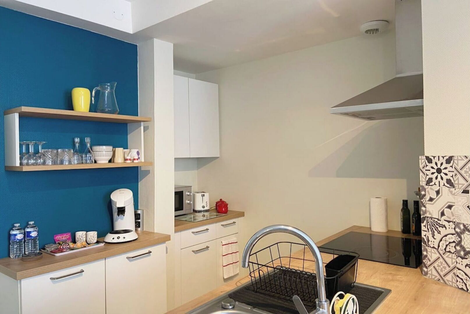 A compact kitchen with white cabinets, a coffee maker, a toaster, and a sink with a dish rack.