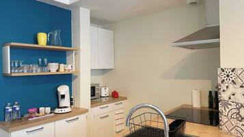 A compact kitchen with white cabinets, a coffee maker, a toaster, and a sink with a dish rack.