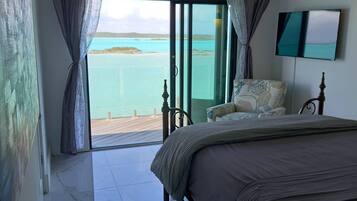 A bedroom with a bed, a chair, a TV, and a view of the sea.