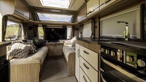 A compact RV interior with a kitchenette, a seating area, and a TV. - 2 Double Bed Caravan - Secure Parking and Wifi (Llandeilo)