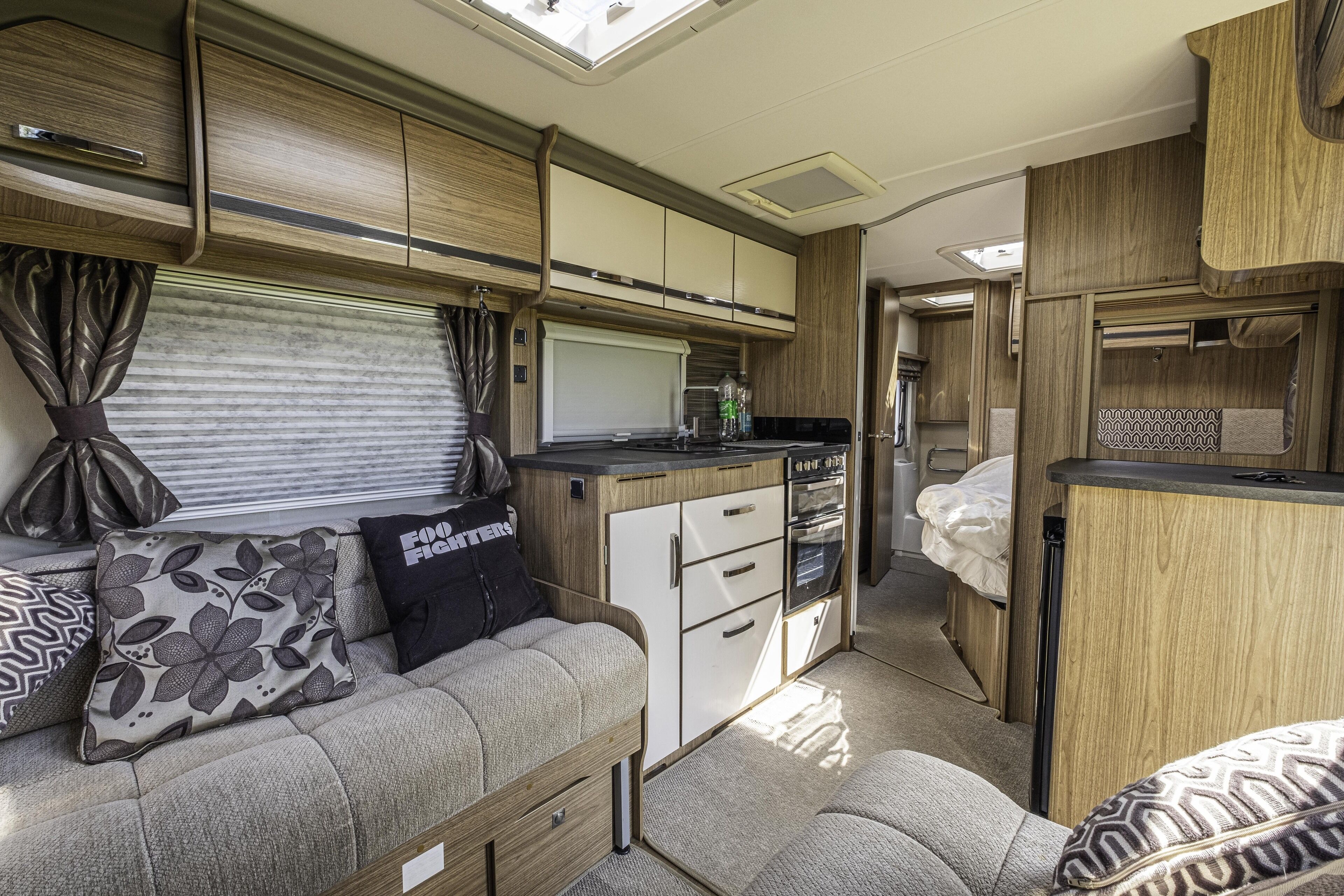 A compact RV interior with a kitchenette, a sofa with patterned cushions, and a small bed area.