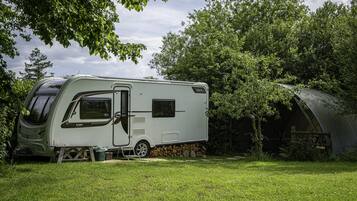 A white RV parked in a grassy area with a covered structure nearby.