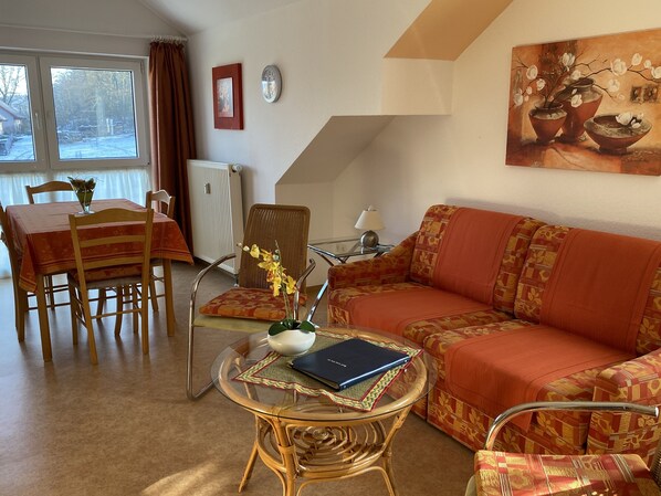 A living room with a sofa, a dining table with chairs, a glass coffee table, and a painting on the wall. - "Fernblick" Vacation Apartment - Hiking, Biking, Golf, Leisure, Relaxation (Schwedelbach)