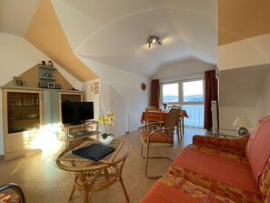 A living room with a sofa, a glass coffee table, a television, and a dining area with a table and chairs. - "Fernblick" Vacation Apartment - Hiking, Biking, Golf, Leisure, Relaxation (Schwedelbach)