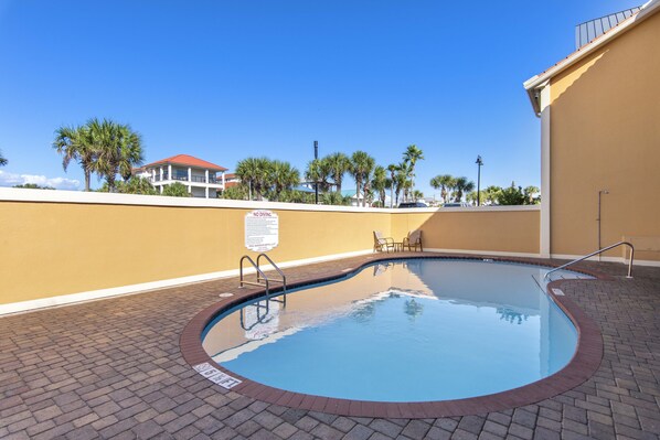 A swimming pool with a no diving sign, surrounded by a brick walkway and palm trees.