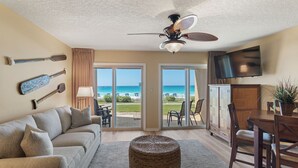 Un salon comprenant un canapé, une table à manger, des chaises, un ventilateur de plafond, un téléviseur et une vue sur l’océan grâce à de grandes portes vitrées.