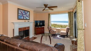 A living room with a fireplace, leather sofa, television, and a view of the ocean. - Ocean Front Condo Shorebirds 83 (Pajaro Dunes)