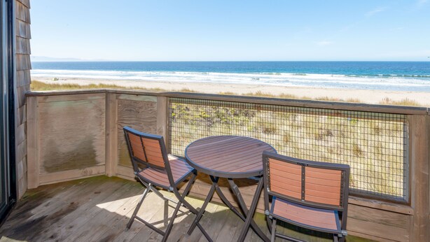 A wooden deck with a table and chairs overlooking a beach. - Ocean Front Condo Shorebirds 83 (Pajaro Dunes)