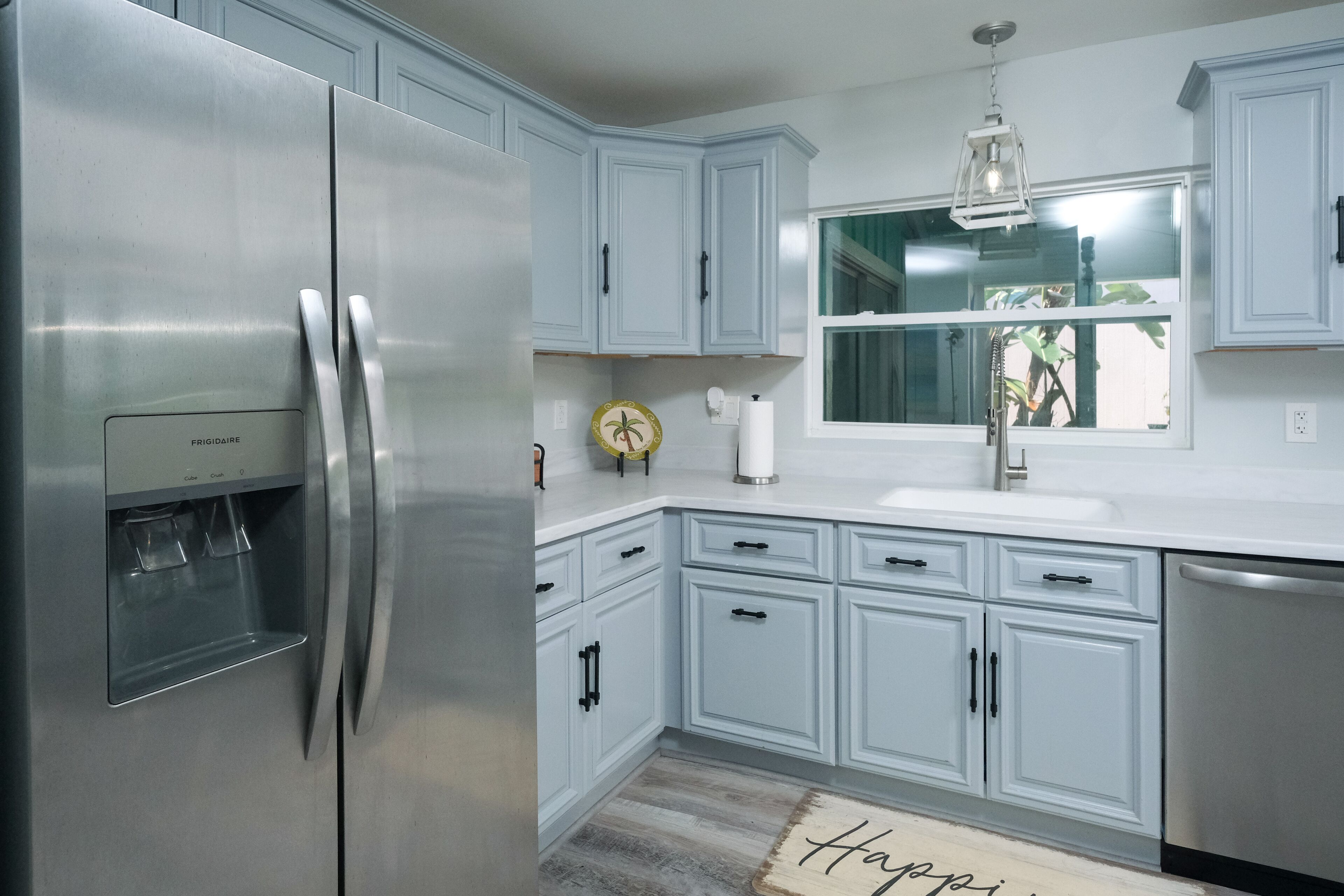 A modern kitchen with light blue cabinets, stainless steel appliances, and a window above the sink.