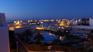 A nighttime view of a resort area with a pool, palm trees, and a distant shoreline. - spacious apartment s + 2 sea view in Hammamet (Hammamet)