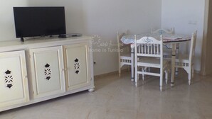 A room with a white cabinet, a television on top, and a table with chairs. - spacious apartment s + 2 sea view in Hammamet (Hammamet)