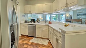 A modern kitchen with white cabinetry, a built-in dishwasher, and a large island with a sink. - Luxury Lagoon View Villa Pool & Tennis Hilton Head (Hilton Head Island)