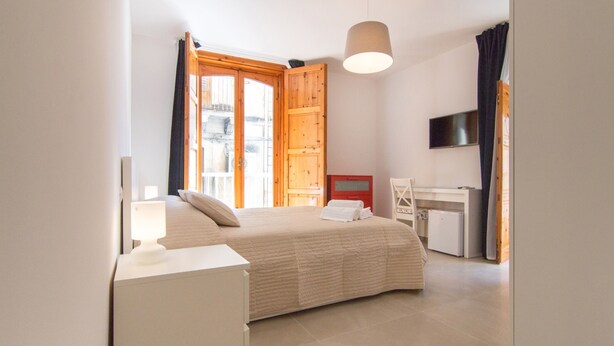 A bedroom with a bed, bedside table, lamp, and a desk with a chair. - HILDE'S HOUSE 1 (Scicli)