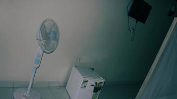A standing fan and a small refrigerator in a room with a tiled floor and a white wall.