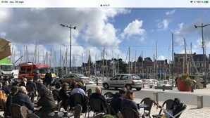 A marina with people seated at outdoor tables, boats docked in the background, and a red emergency vehicle parked nearby. - Cœur de Paimpol 54 m2 (Paimpol)