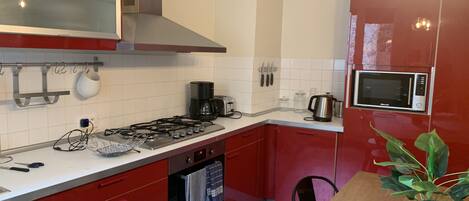 A modern kitchen with red cabinets, a stainless steel range hood, a microwave, and a coffee maker.