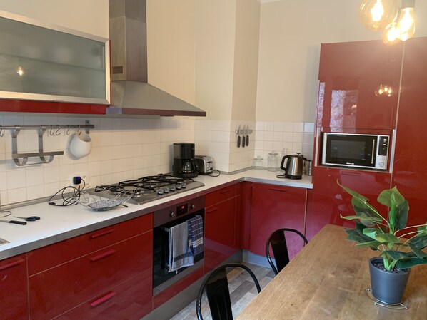A modern kitchen with red cabinets, a stainless steel range hood, a microwave, and a coffee maker.
