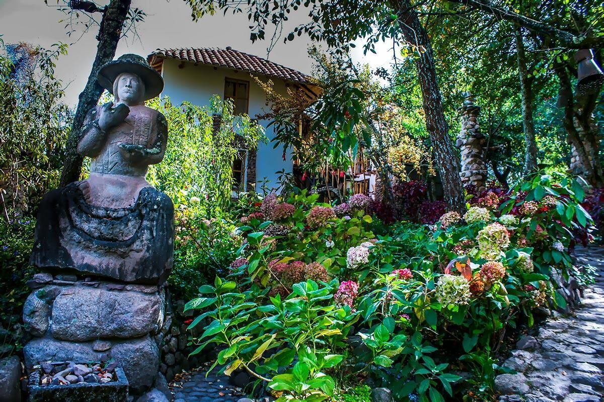 A garden with a stone statue, lush greenery, and a building in the background.