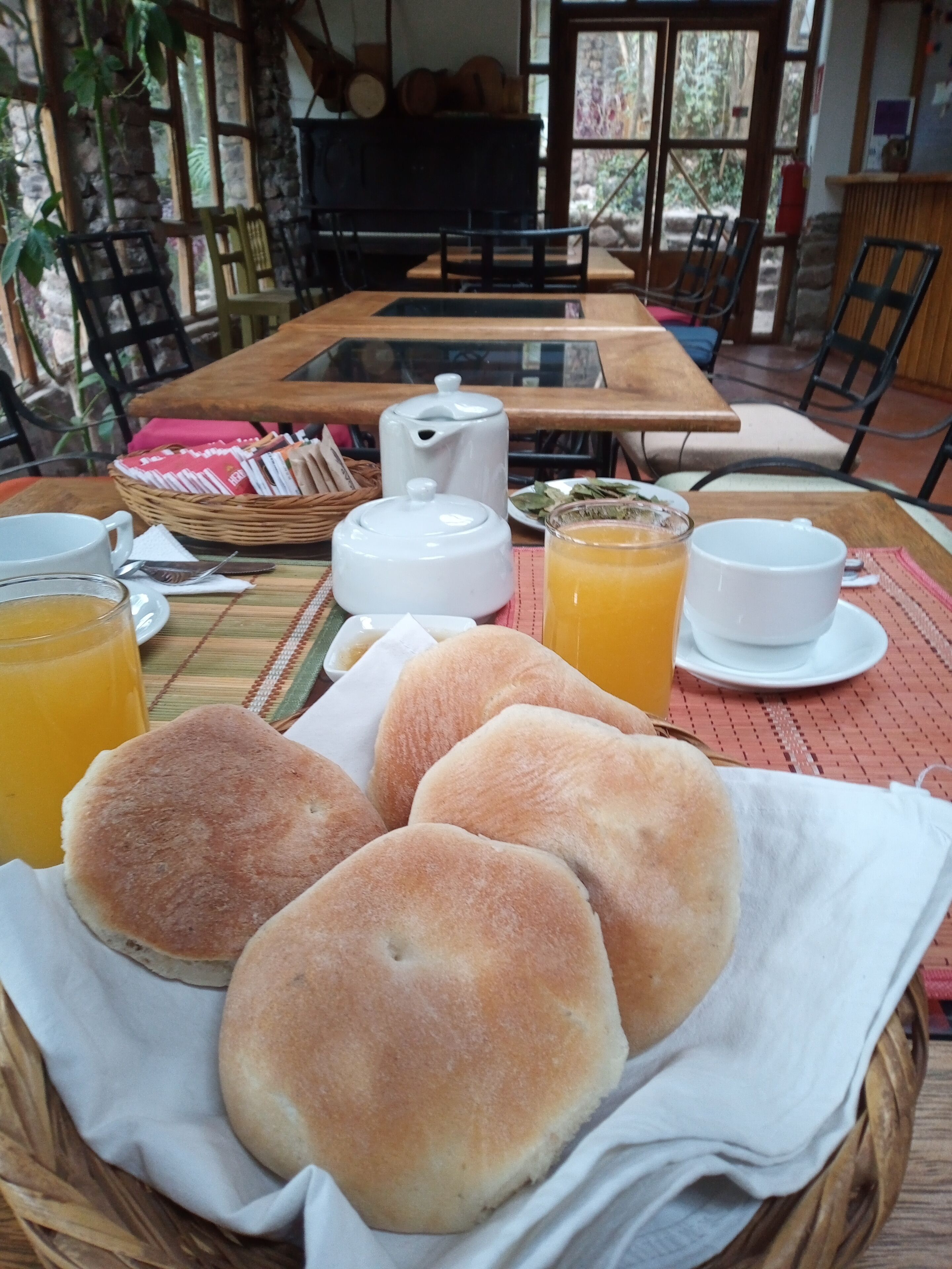 Ein Frühstückstisch mit Brötchen, Orangensaft und einer weißen Teekanne.