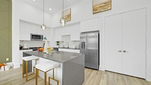 A modern kitchen with white cabinetry, stainless steel appliances, and a central island with bar stools.