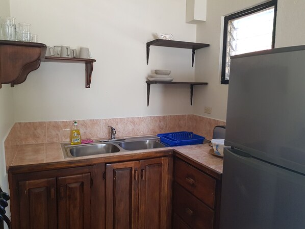 Una cocina con gabinetes de madera, un lavamanos de acero inoxidable y un refrigerador negro.