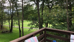Une terrasse en bois avec un banc et une table, donnant sur un espace verdoyant planté d’arbres.