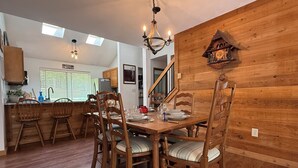 Un coin repas avec des chaises en bois et une table dressée pour quatre personnes, un lustre et un mur en bois orné d’une horloge.