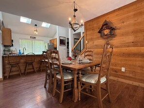 A dining area with wooden chairs and a table set for four, a chandelier, and a wooden wall with a clock.