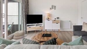 Una sala de estar moderna con un televisor de pantalla plana, una mesa de centro de madera y un sofá gris.