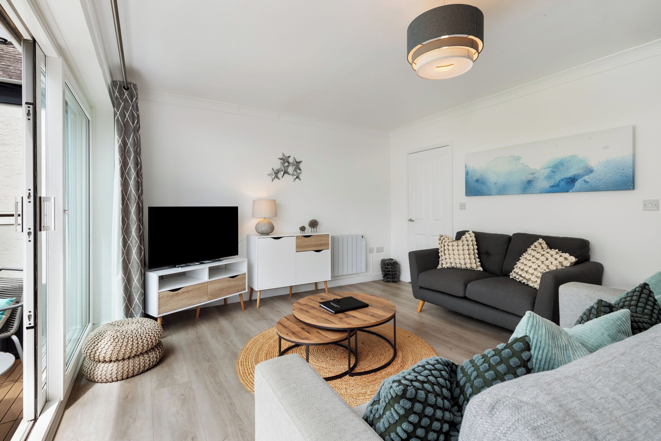 A modern living room with a flat-screen TV, a sofa, a coffee table, and a dining area with a table and chairs.