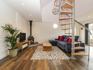 Una sala de estar moderna con piso de madera, una chimenea empotrada, una escalera curva y un ventanal grande.
