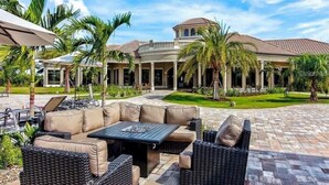 Un patio con mobiliario exterior, palmeras y un edificio de techo a tejas.