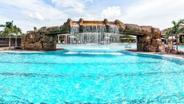 Una piscina con una cascada, rodeada de palmeras y sillas de descanso.