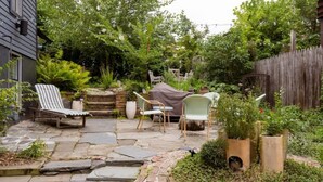 Une terrasse en pierre avec des meubles d’extérieur, entourée d’une végétation luxuriante et d’une clôture en bois.