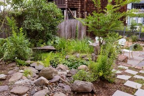 Stroll through the serene garden, surrounded by lush plants and a tranquil pond, with a wooden deck and seating area inviting relaxation.