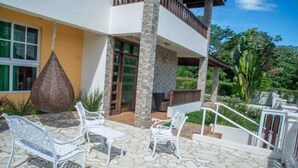 Une maison moderne dotée d’un patio en pierre, de mobilier d’extérieur blanc et d’un balcon.