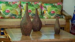 Une table en bois, trois vases et un canapé agrémenté d’un coussin à motifs tropicaux.