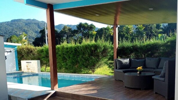 Un espace extérieur moderne doté d’une piscine, d’un revêtement de sol en bois et d’un coin salon couvert avec un canapé et une table.