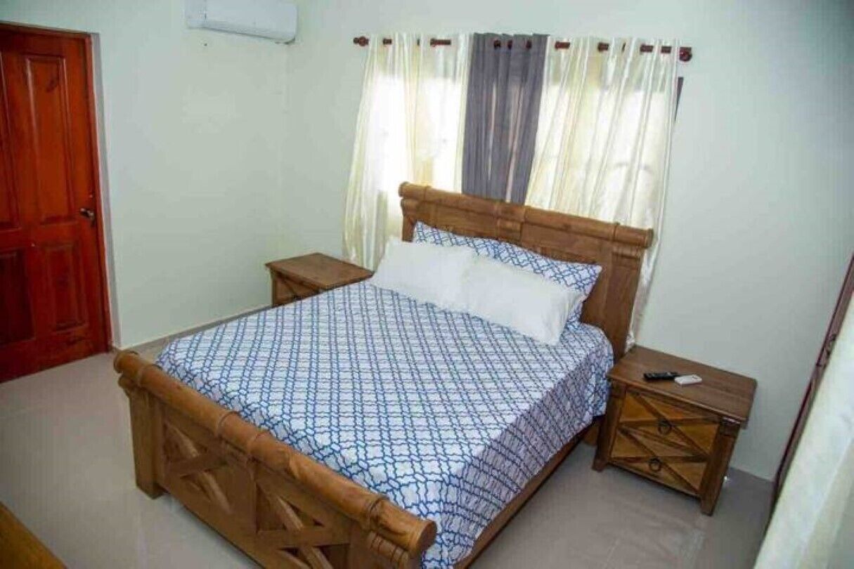 A bedroom with a wooden bed, a nightstand, a bedside table, and a window with curtains.