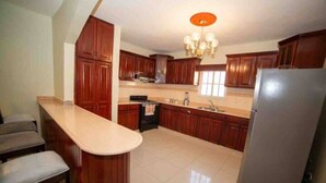 A kitchen with wooden cabinets, a stainless steel refrigerator, and a bar counter.