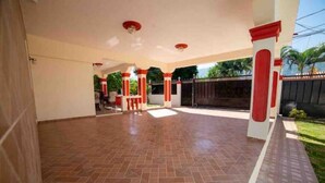 A spacious covered patio with red and white pillars, a tiled floor, and a view of a gated area with greenery.