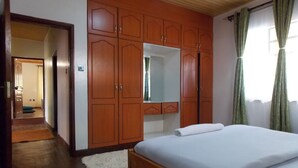 A bedroom with a wooden wardrobe, a bed with white bedding, a mirror, and a window with curtains. - Stunning Villa in Private Compound in Nairobi, KE (Ongata Rongai)