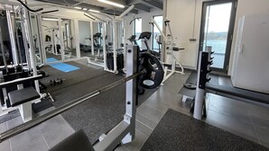 A gym with various exercise equipment, a blue mat, and a view of the water through the windows. - Modernes Apartment mit Wunderschönem Rheinblick (Urmitz)