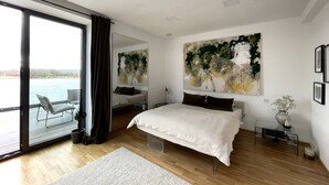 A modern bedroom with a large bed, a view of the outdoors, and a sliding glass door leading to a balcony. - Modernes Apartment mit Wunderschönem Rheinblick (Urmitz)